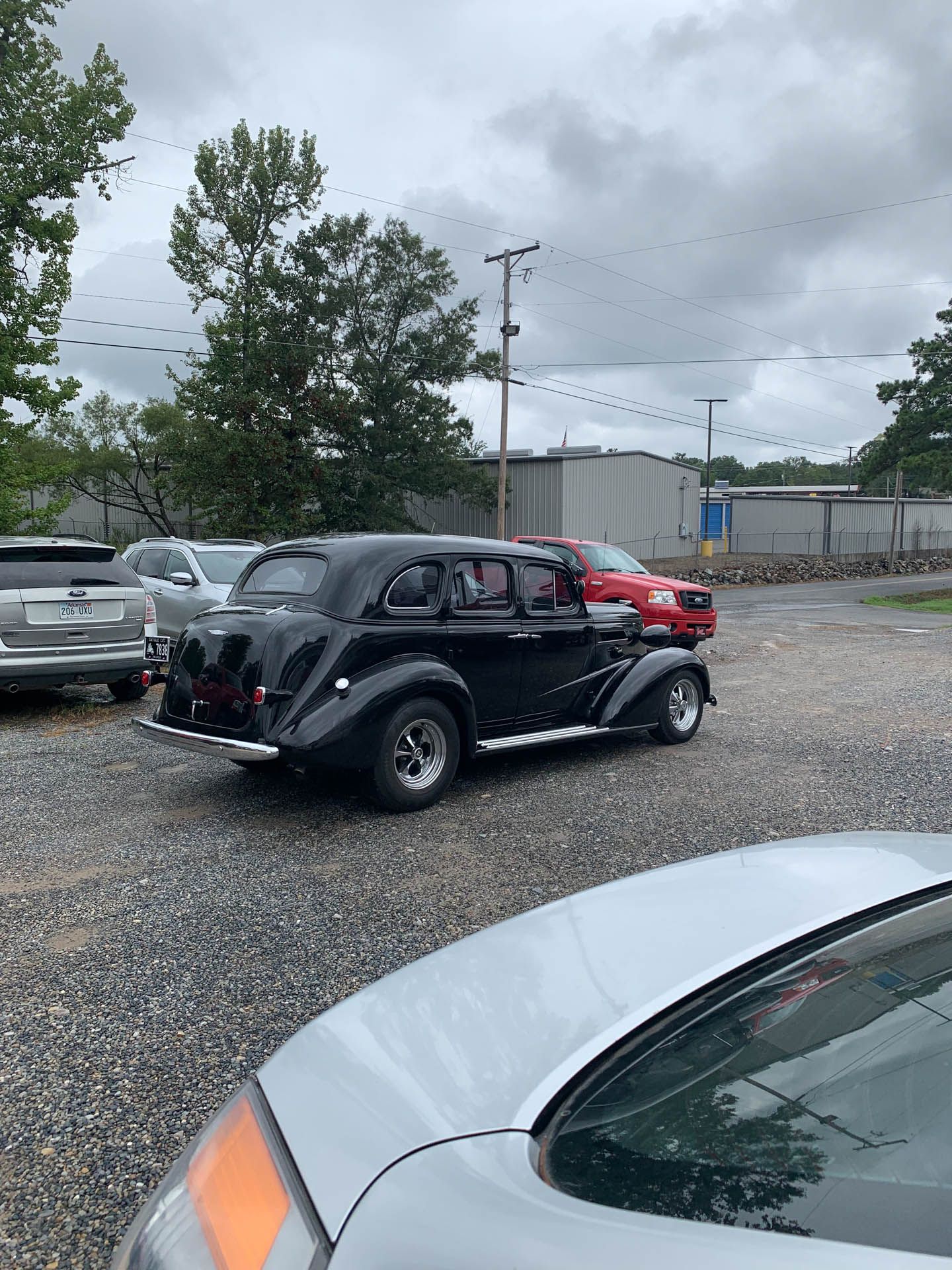 A black car is parked in a gravel lot next to a silver car.