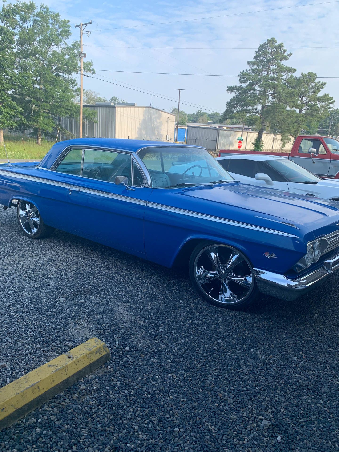 A blue car is parked in a gravel lot.