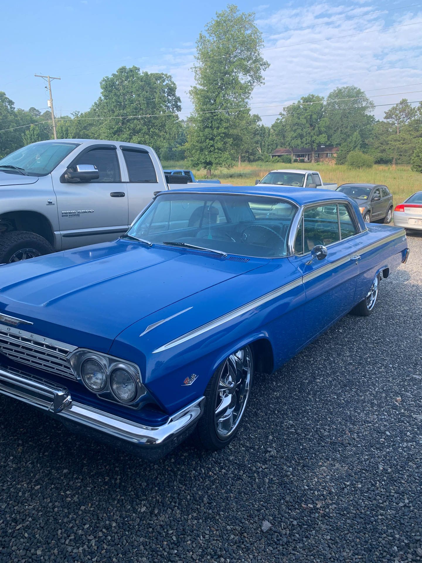 A blue car is parked in a gravel lot next to a truck.