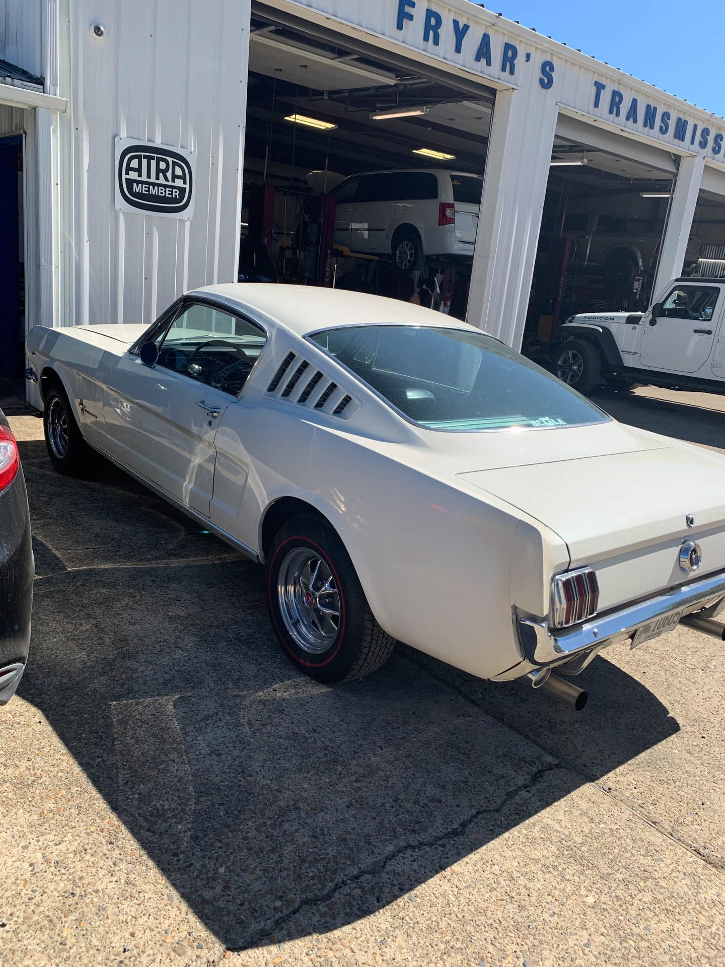 A white mustang is parked in front of a garage.