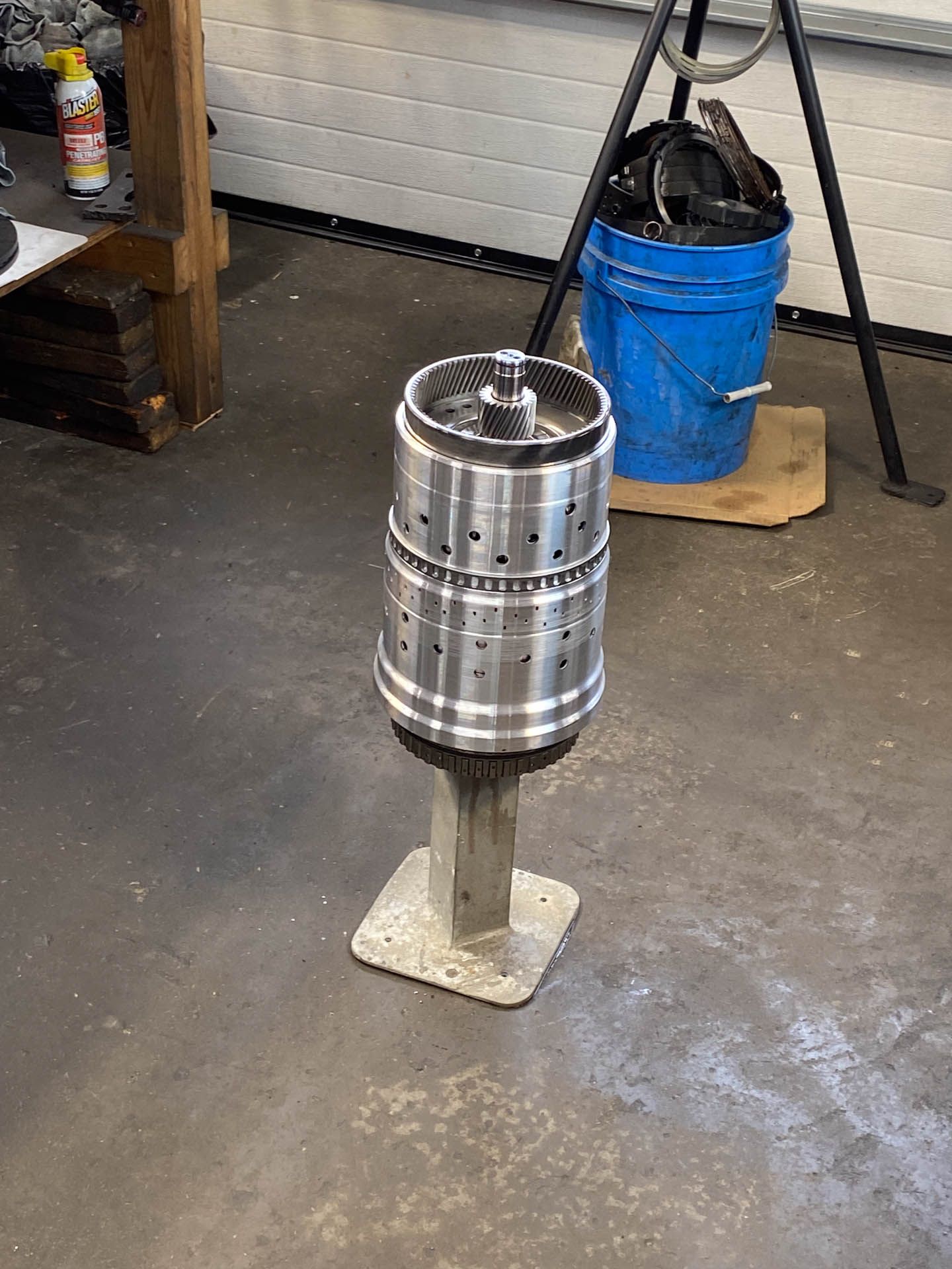 A metal object is sitting on a pedestal in a garage next to a blue bucket.