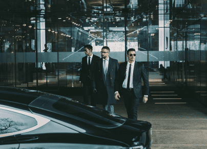 Three men in suits and ties are walking next to a black car.