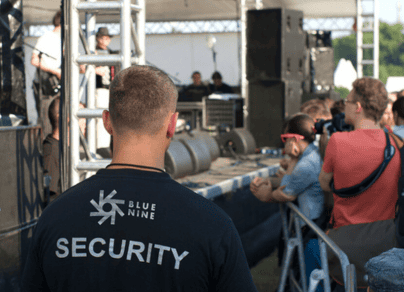 A man wearing a security shirt stands in front of a crowd