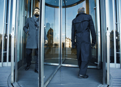 Two men are walking out of a revolving door.