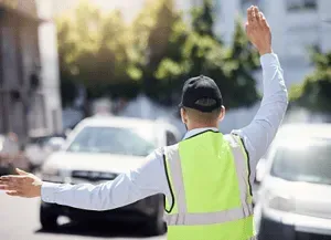 A man in a yellow vest is standing in the middle of a street.