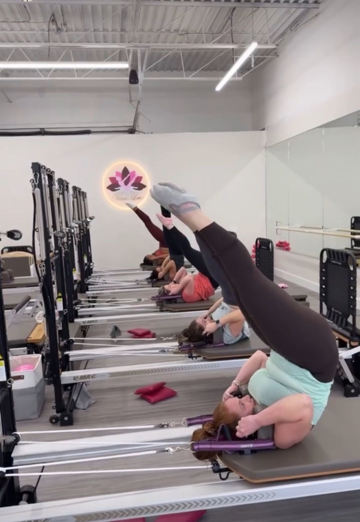 A group of women are doing stretching exercises on pilates machines in front of a mirror.