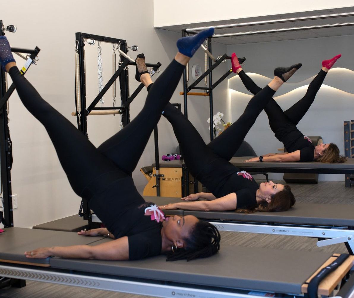 Three people doing Pilates leg exercises on reformers in a studio.