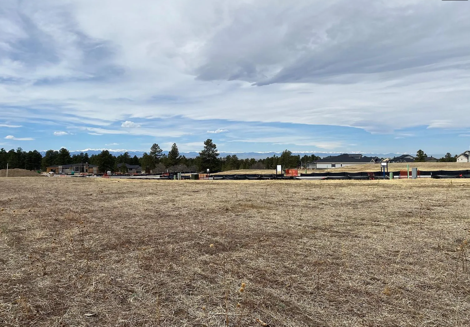 A wide, empty field with construction in the background under a cloudy sky.