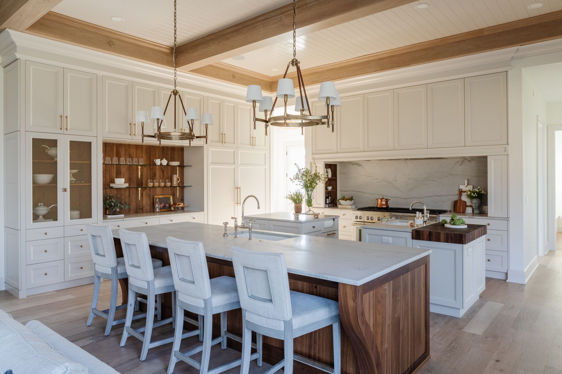 Spacious white kitchen with island seating, wooden accents, and chandeliers.