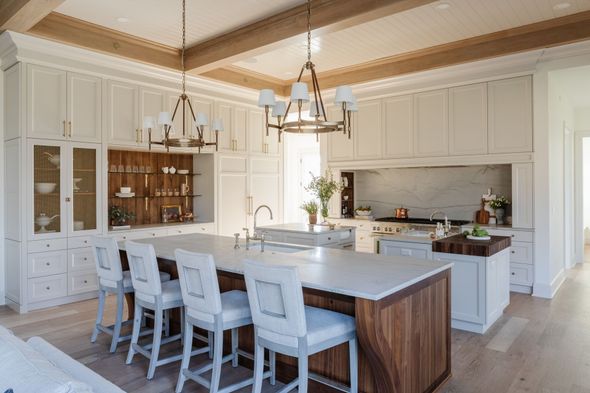 Spacious white kitchen with island seating, wooden accents, and chandeliers.