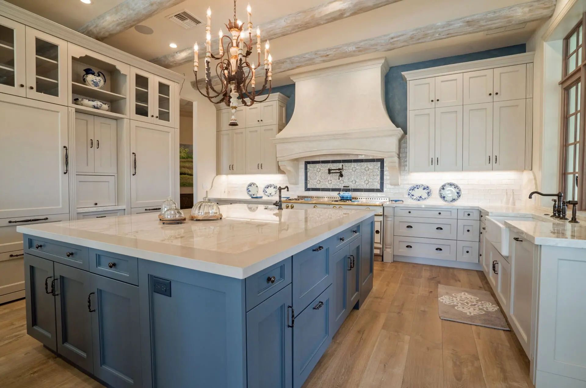 Spacious kitchen with blue island, white cabinets, chandelier, and wooden floor.