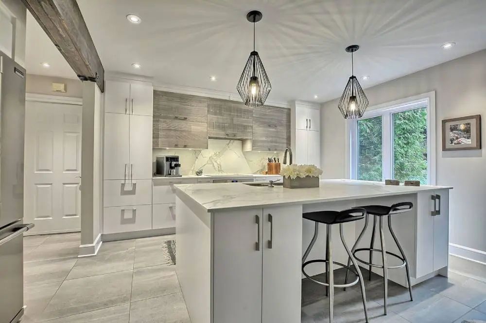 Modern white kitchen with a large island, pendant lights, and stainless steel appliances.