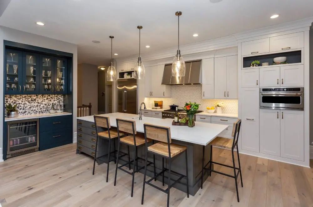 Modern kitchen with gray island, white cabinets, and wooden floors.