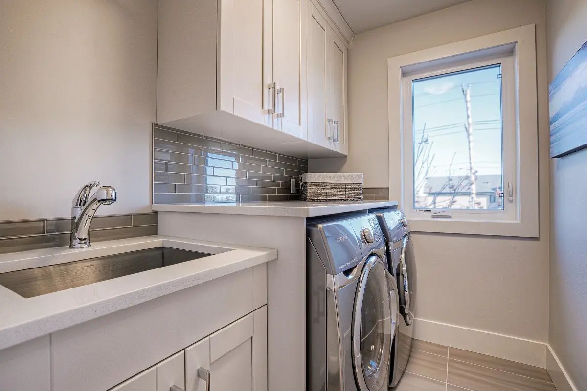 Laundry room with a washing machine, sink, and upper cabinets. Sunlight streams through a window.