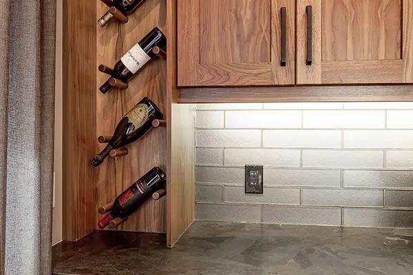 Built-in wine rack with three bottles, beside wooden cabinets and a tiled backsplash.