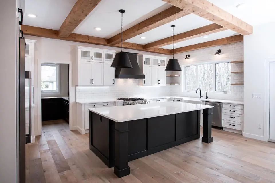 Modern kitchen with white cabinets, black island, wood beams, and pendant lights.