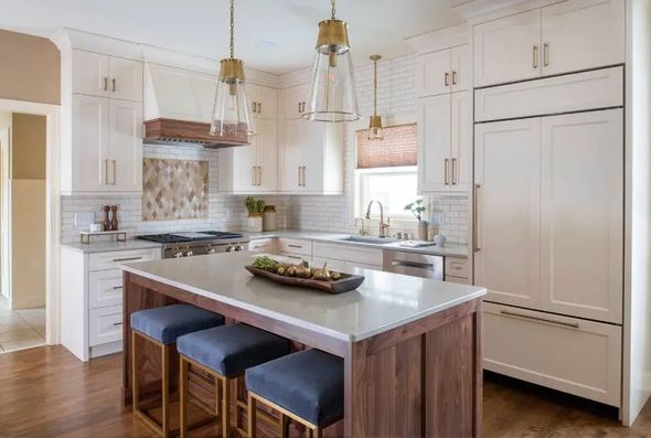 Modern kitchen with white cabinets, wooden island, blue stools, and brass light fixtures.