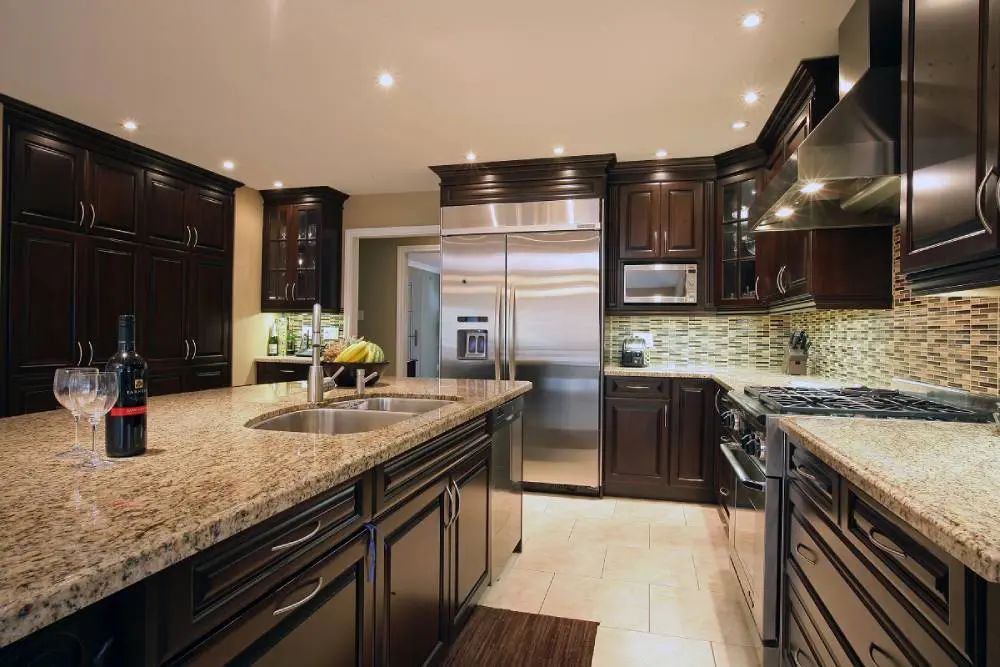 Dark wood kitchen with granite countertops, stainless steel appliances, and tile backsplash.