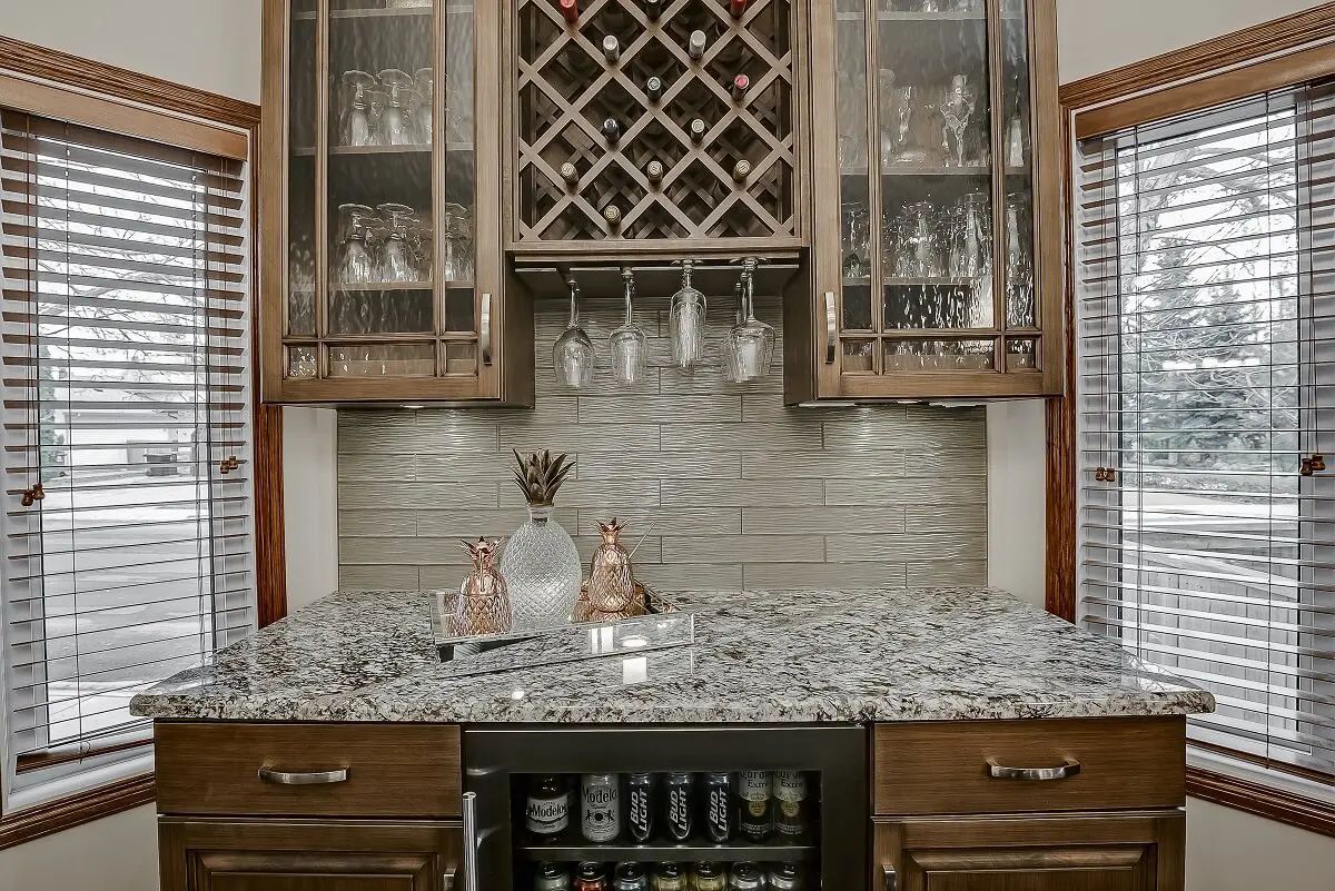 Home bar with cabinets, wine rack, and granite countertop. Windows on either side.