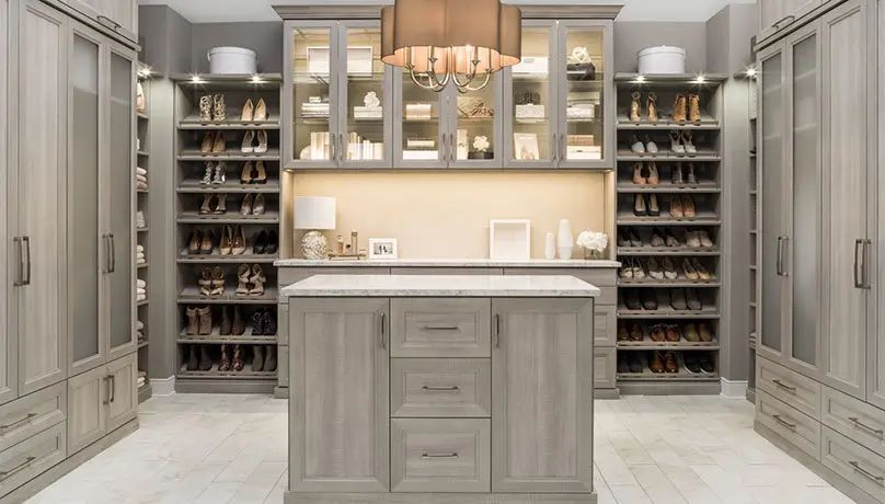 Walk-in closet with gray cabinetry, shoe racks, central island, and chandelier.