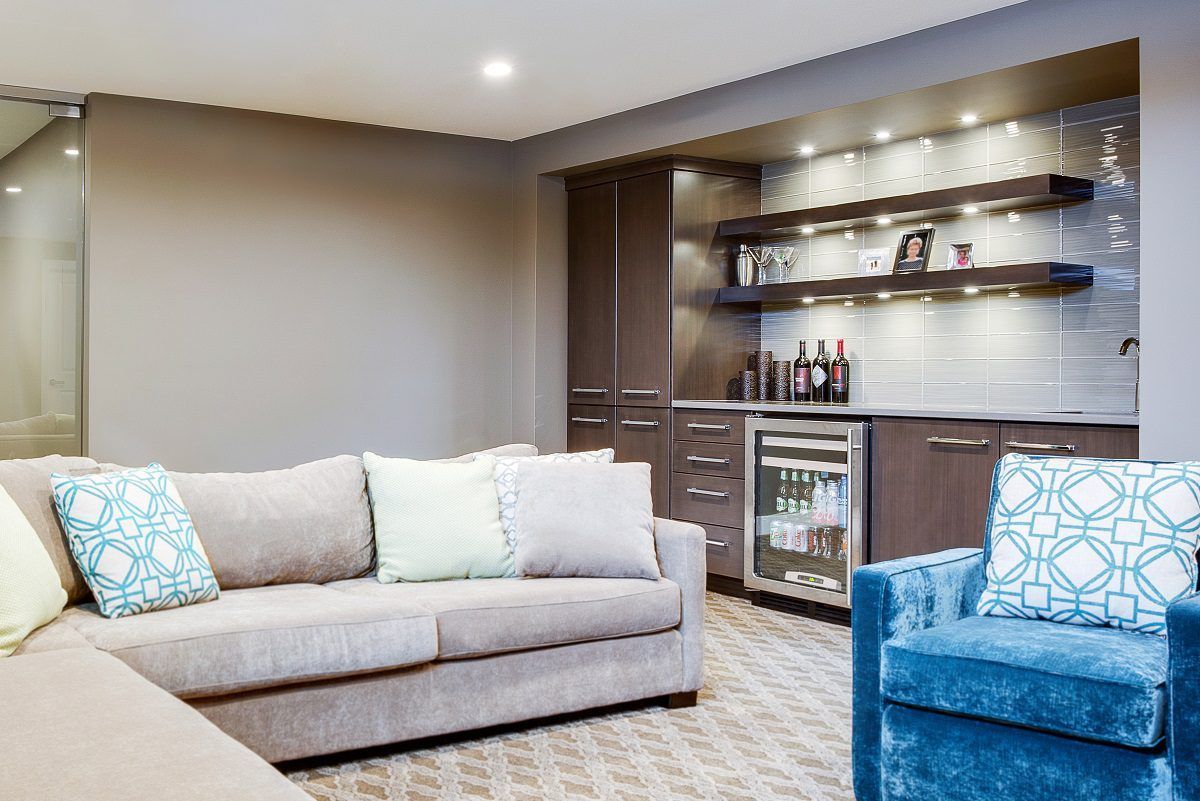 Cozy basement lounge area with a bar, couch, and accent chair in shades of brown, gray, and teal.