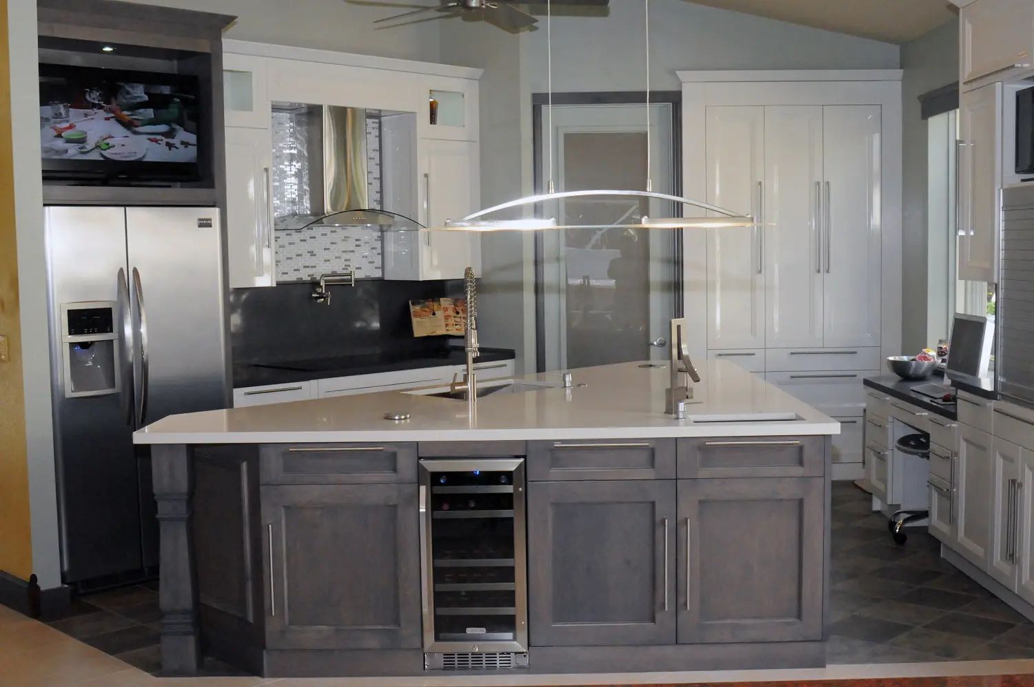 Modern kitchen with gray island, wine fridge, stainless steel appliances, and white cabinets.