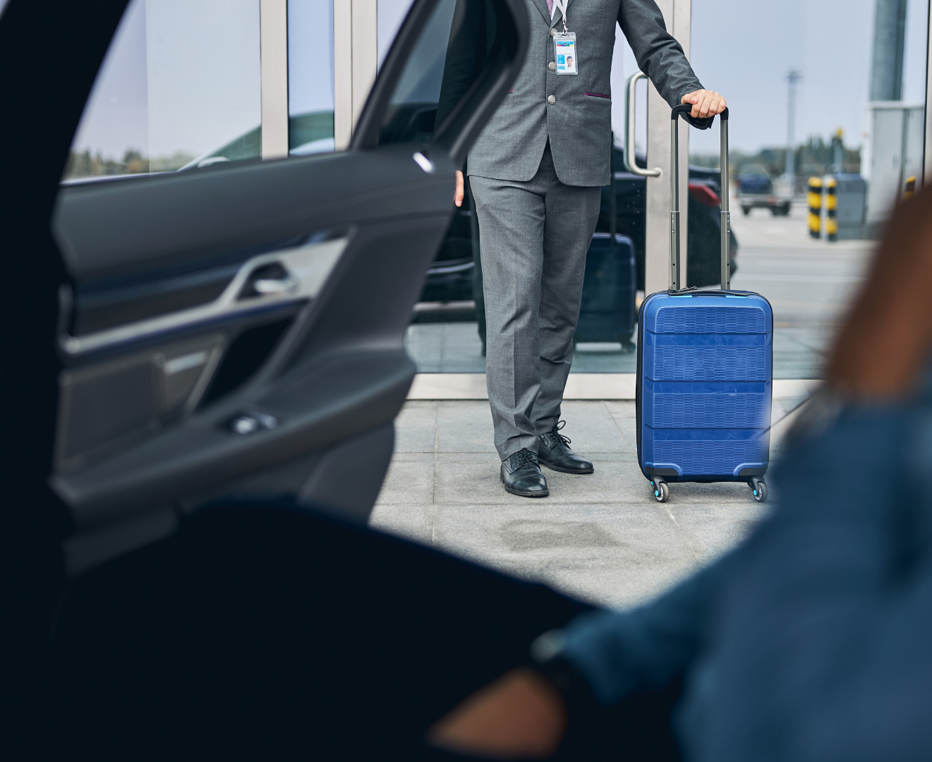 A man in a suit is standing next to a blue suitcase.