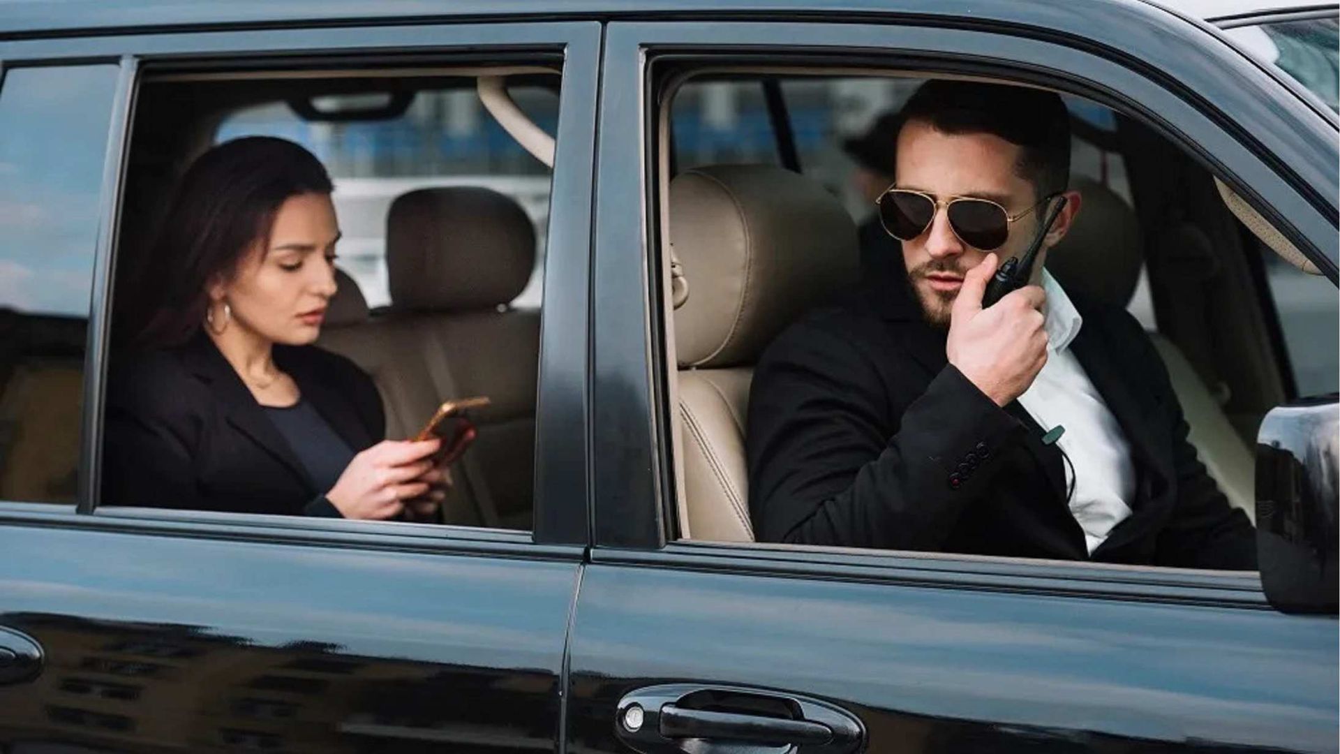 A man and a woman are sitting in a car and the woman is looking at her phone.