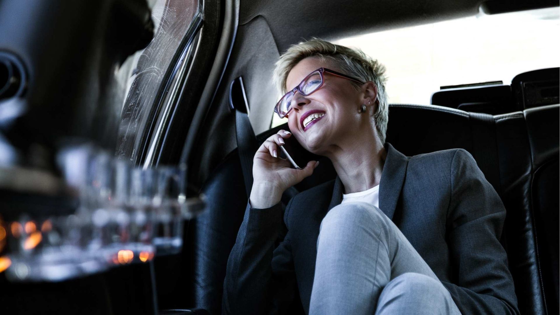 A woman is sitting in the back seat of a car talking on a cell phone.