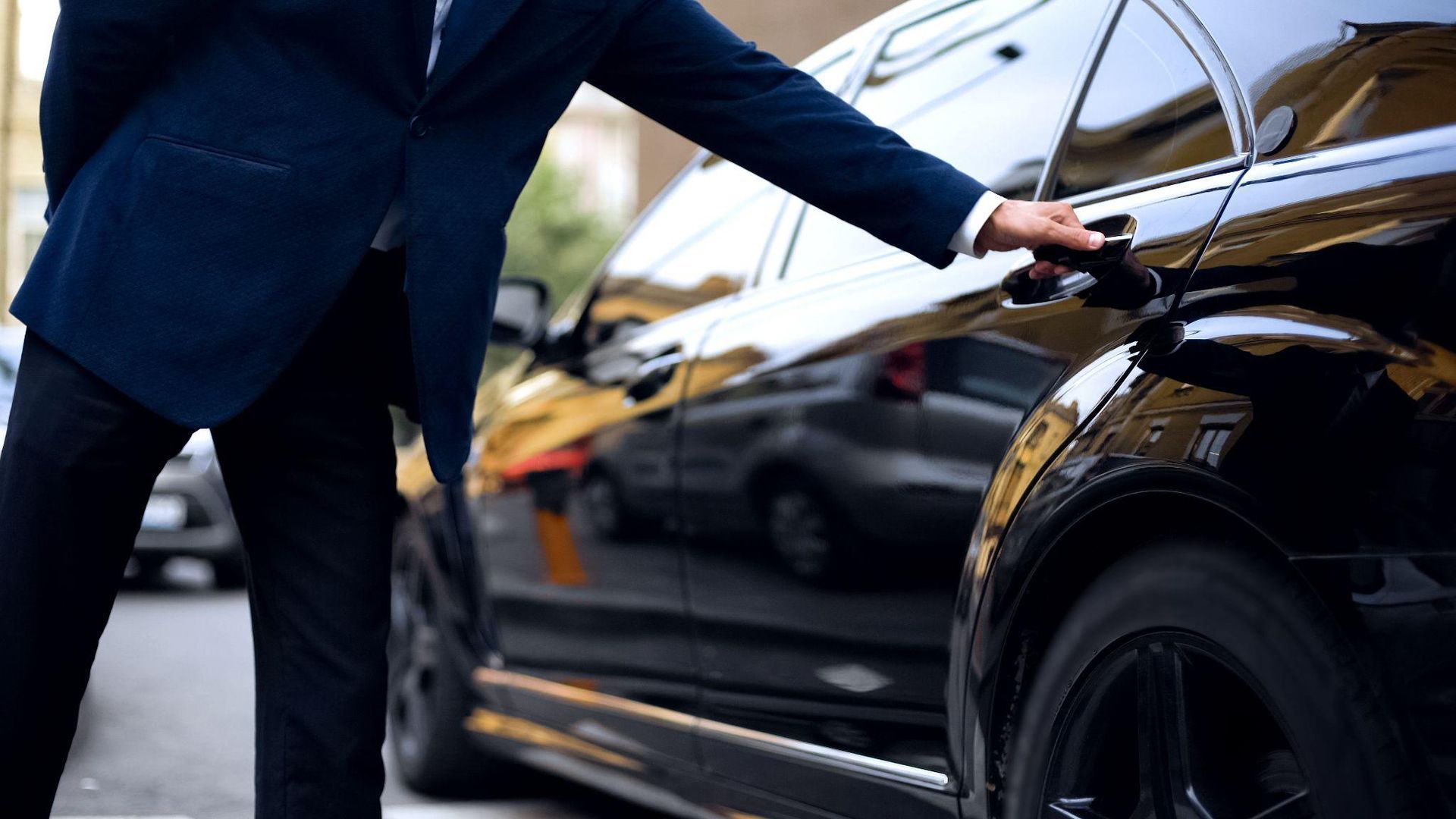 A man in a suit is opening the door of a black car.