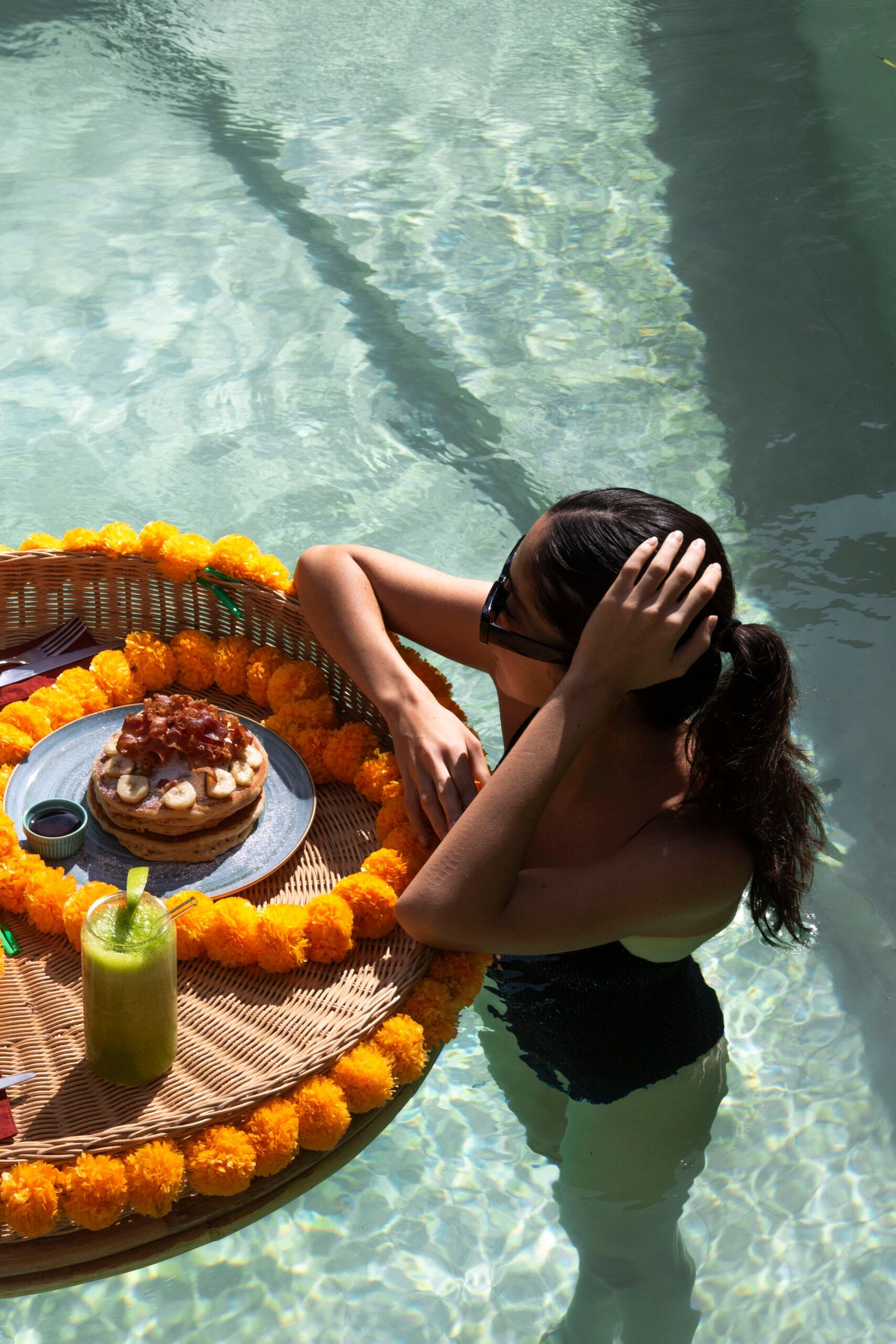 Una mujer está sentada en una piscina con una bandeja de comida y bebidas.