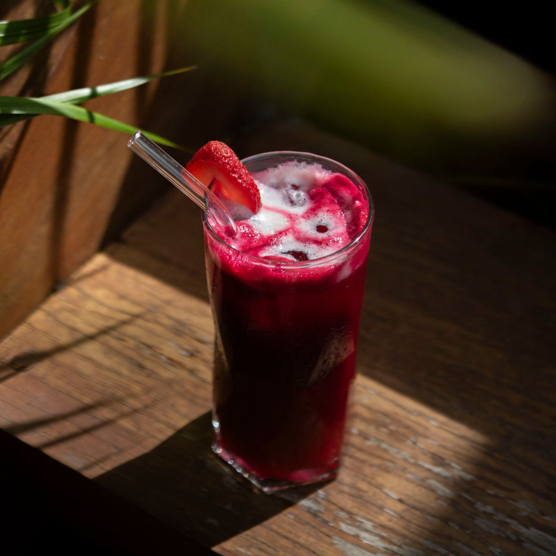 Un vaso de líquido rojo con una pajita y una fresa dentro.