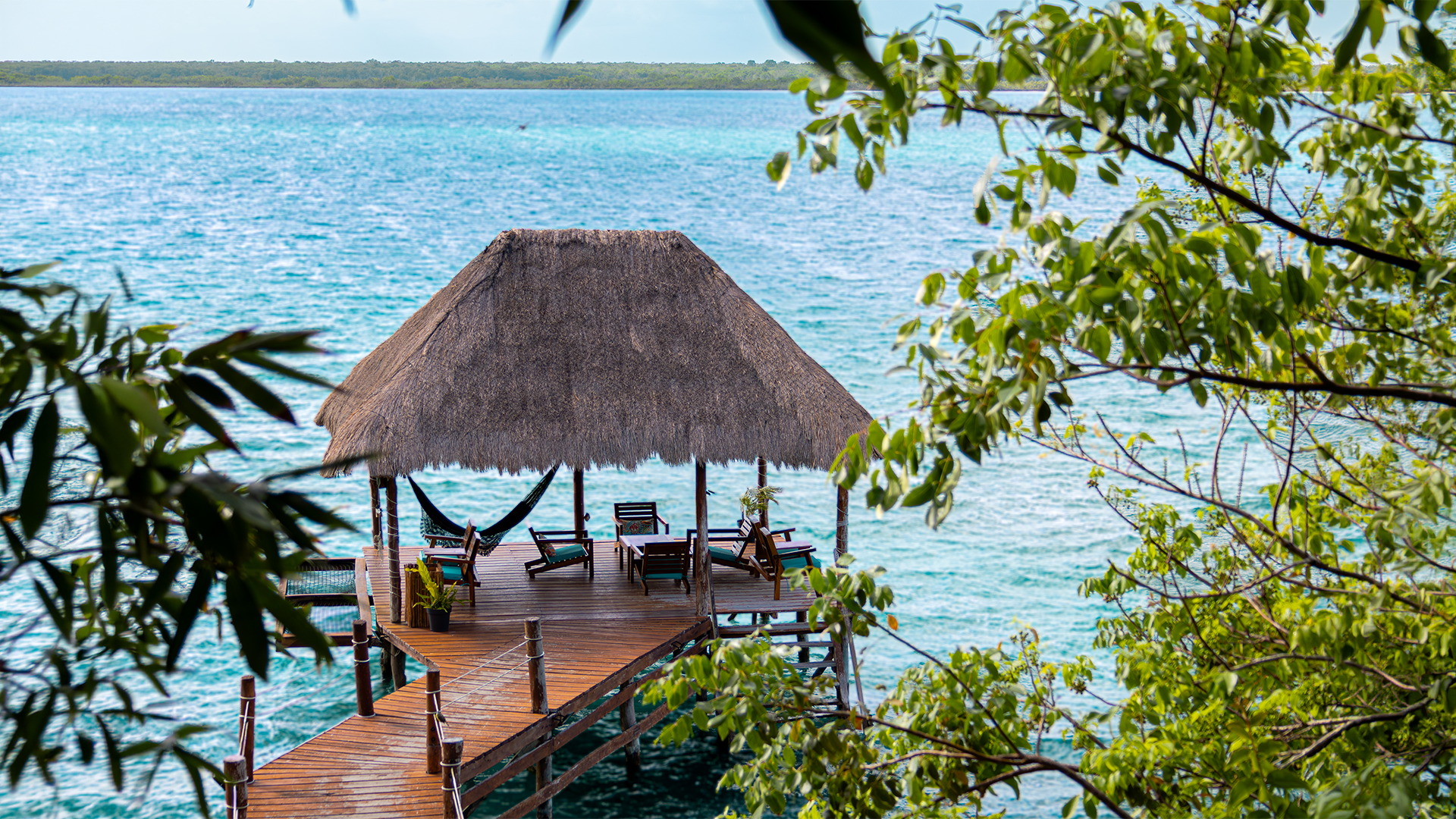 Khaban Bacalar's dock featuring a palapa, hammocks, and lounge chairs overlooking the Bacalar Lagoon.