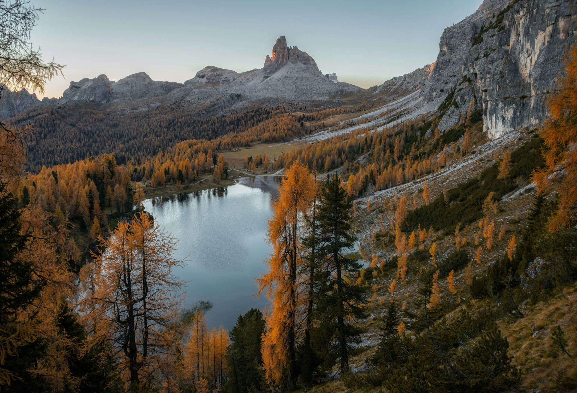 Lake surrounded by autumnal trees and mountains at dusk.