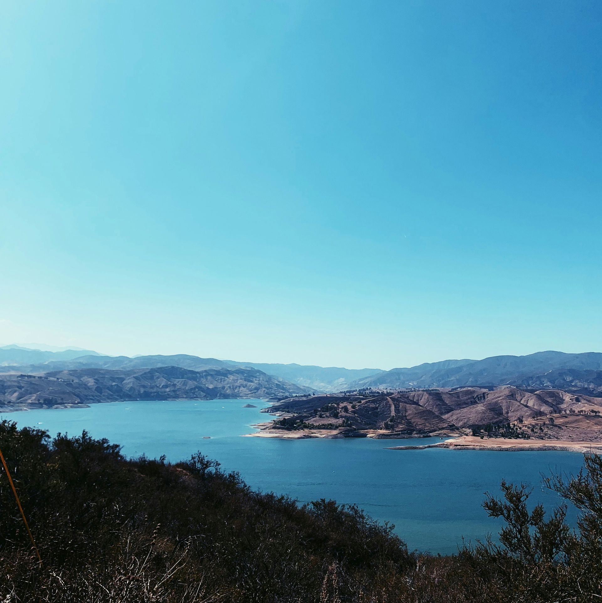 Blue sky over a lake surrounded by dry, brown hills. View from a hillside.