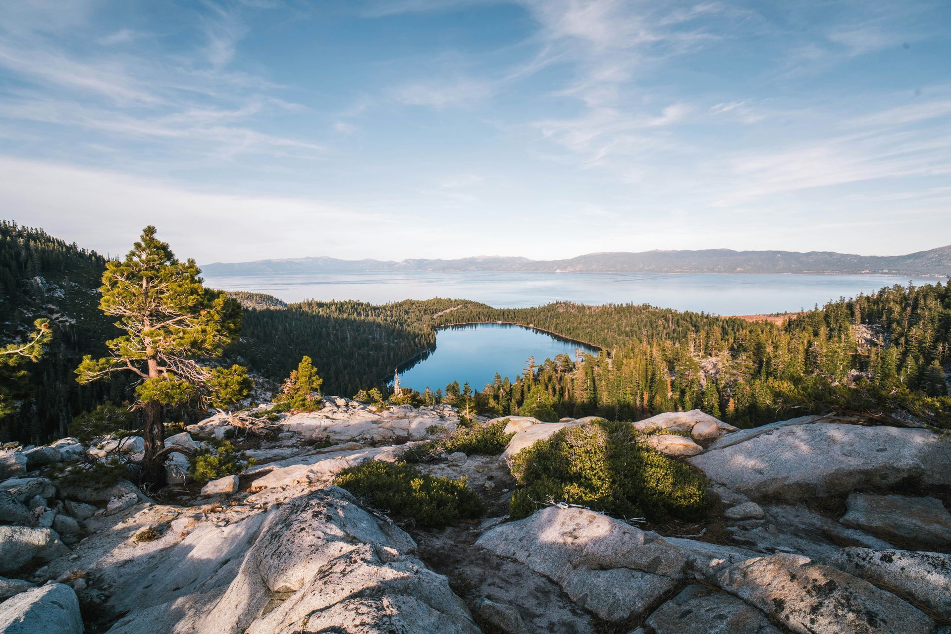 Scenic view of a lake surrounded by trees and mountains under a blue sky.