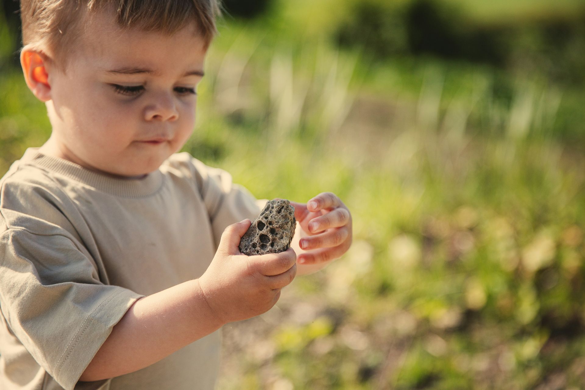 Young child examining a rock outdoors.