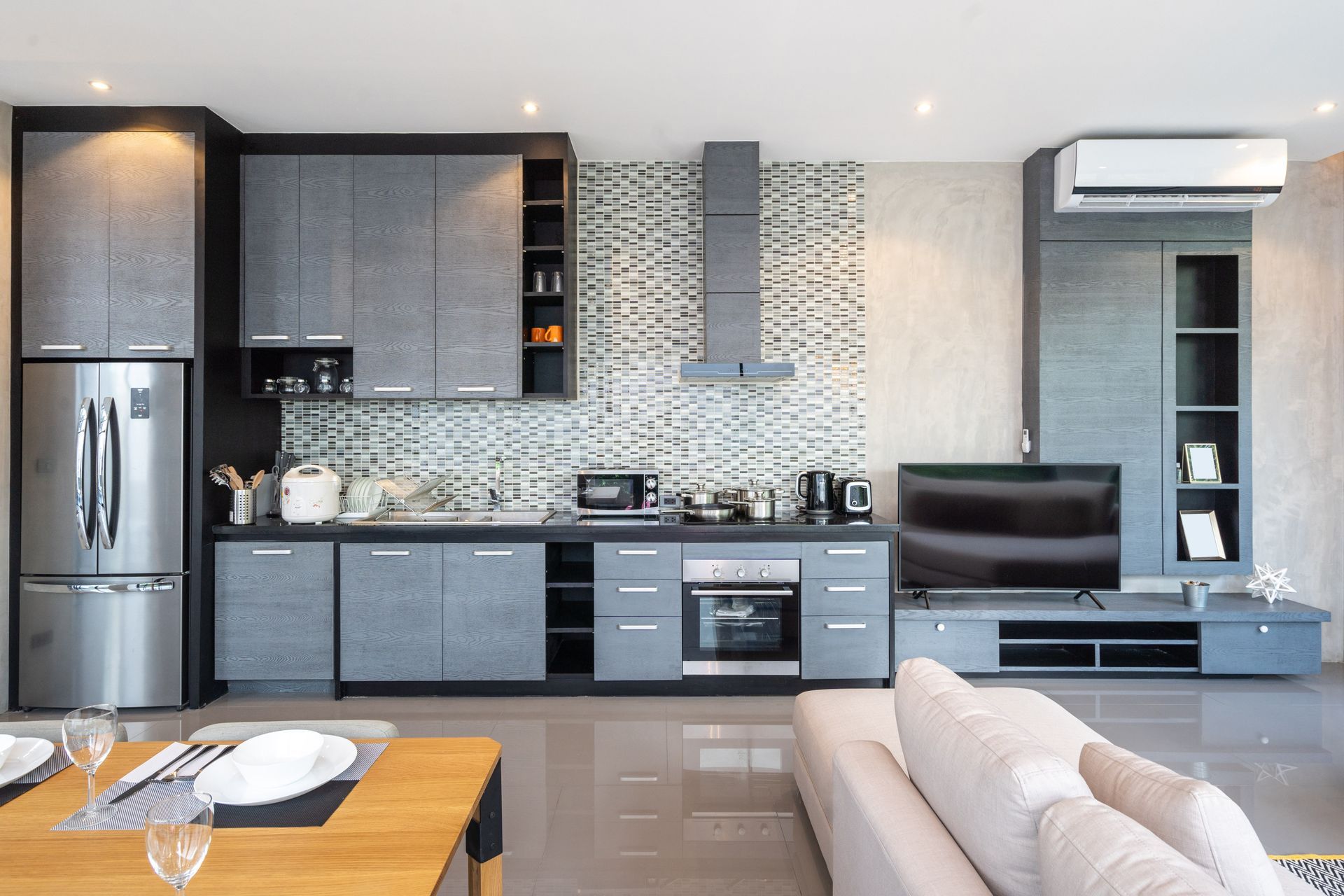 Modern kitchen with gray cabinets, stainless steel appliances, and a living area with a sofa.