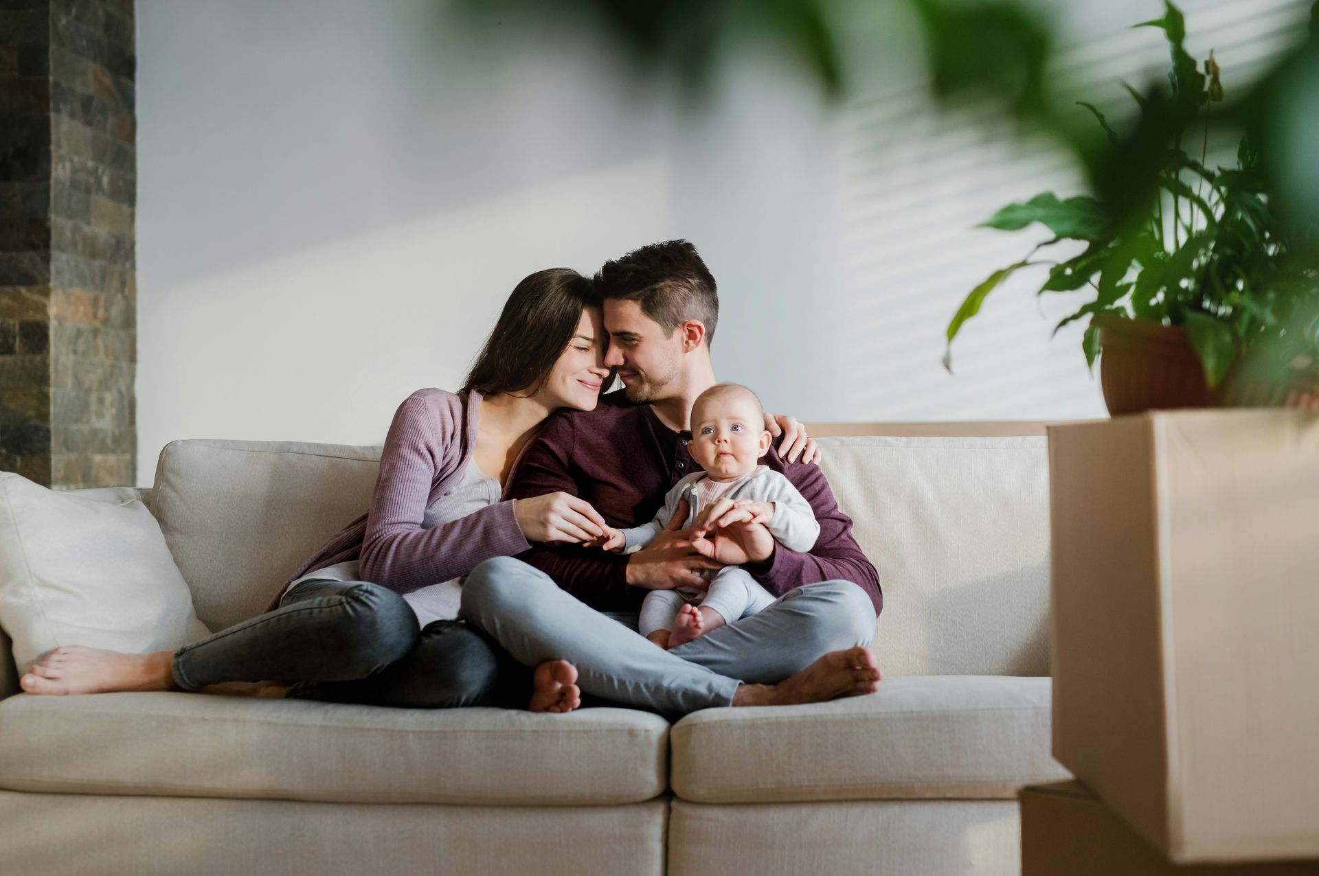 A family of three sits on a couch together, embracing.