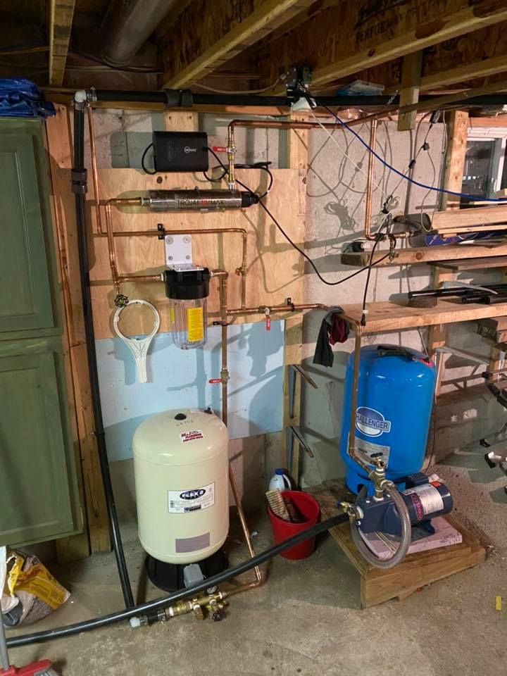 A water pump is sitting in a basement next to a water tank.