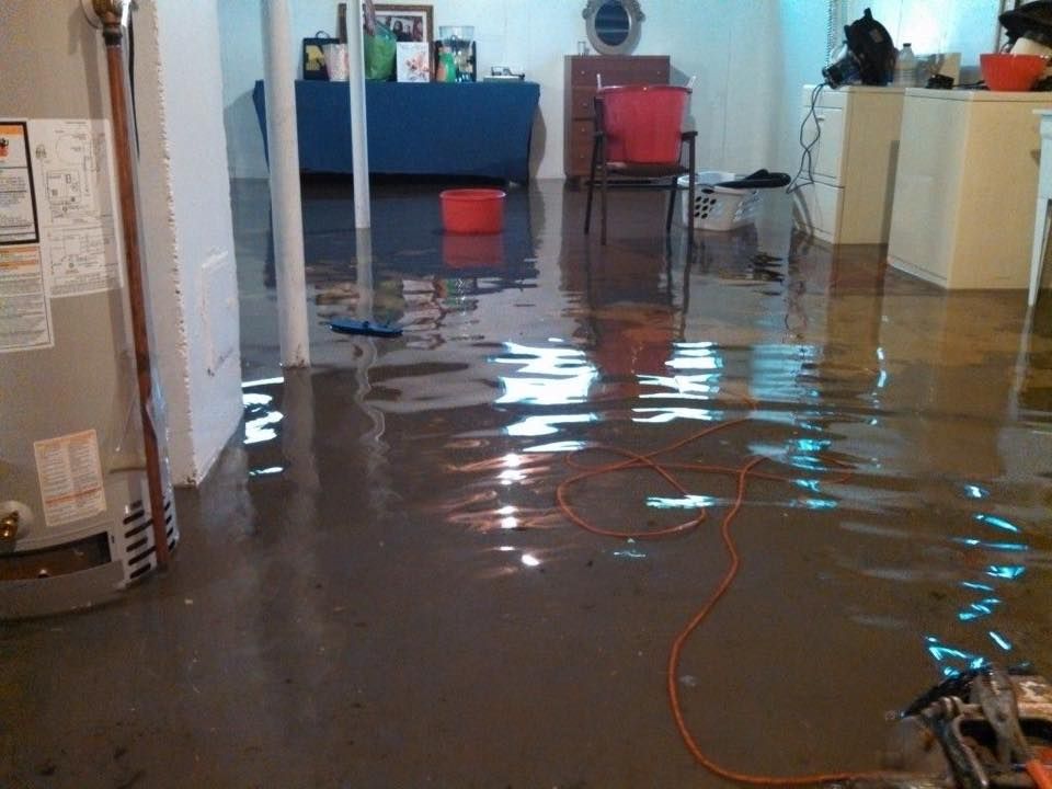A flooded basement with a water heater and a vacuum cleaner