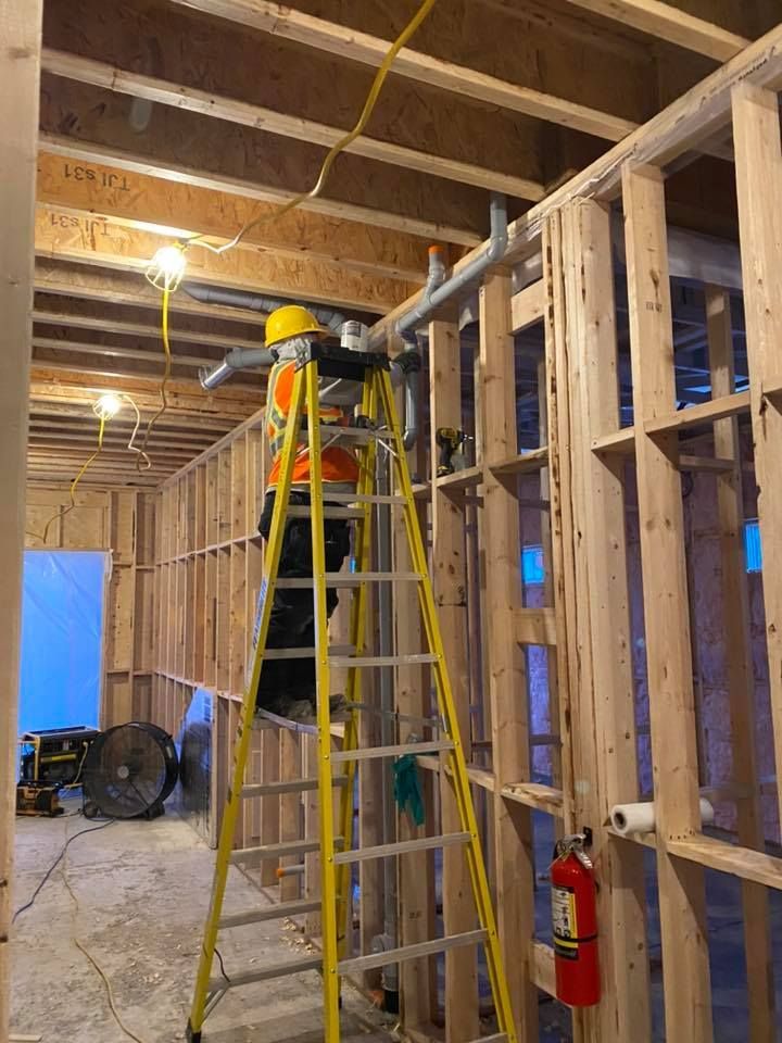 A man is standing on a ladder in a room under construction.