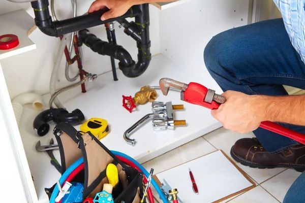 A man is fixing a sink with a wrench.