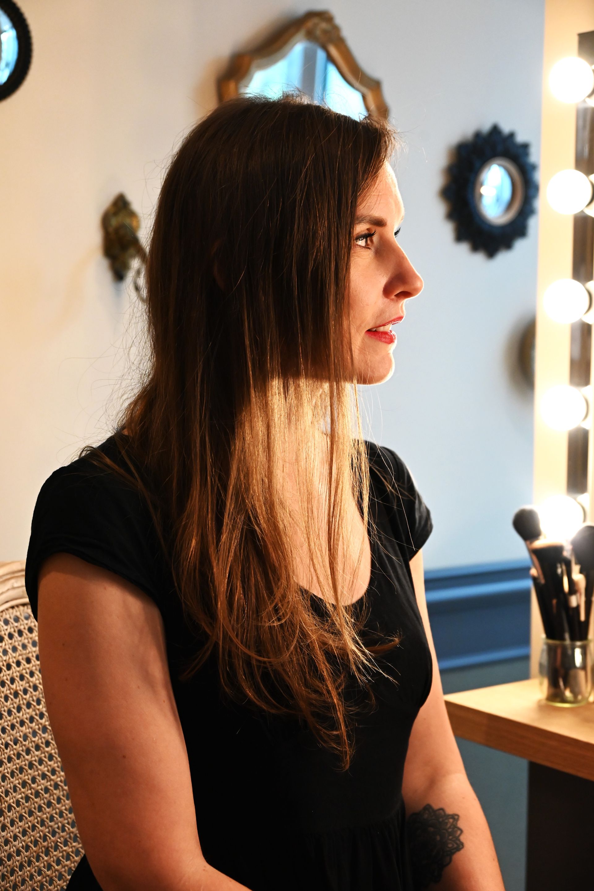 Une femme en chemise noire sourit devant un miroir