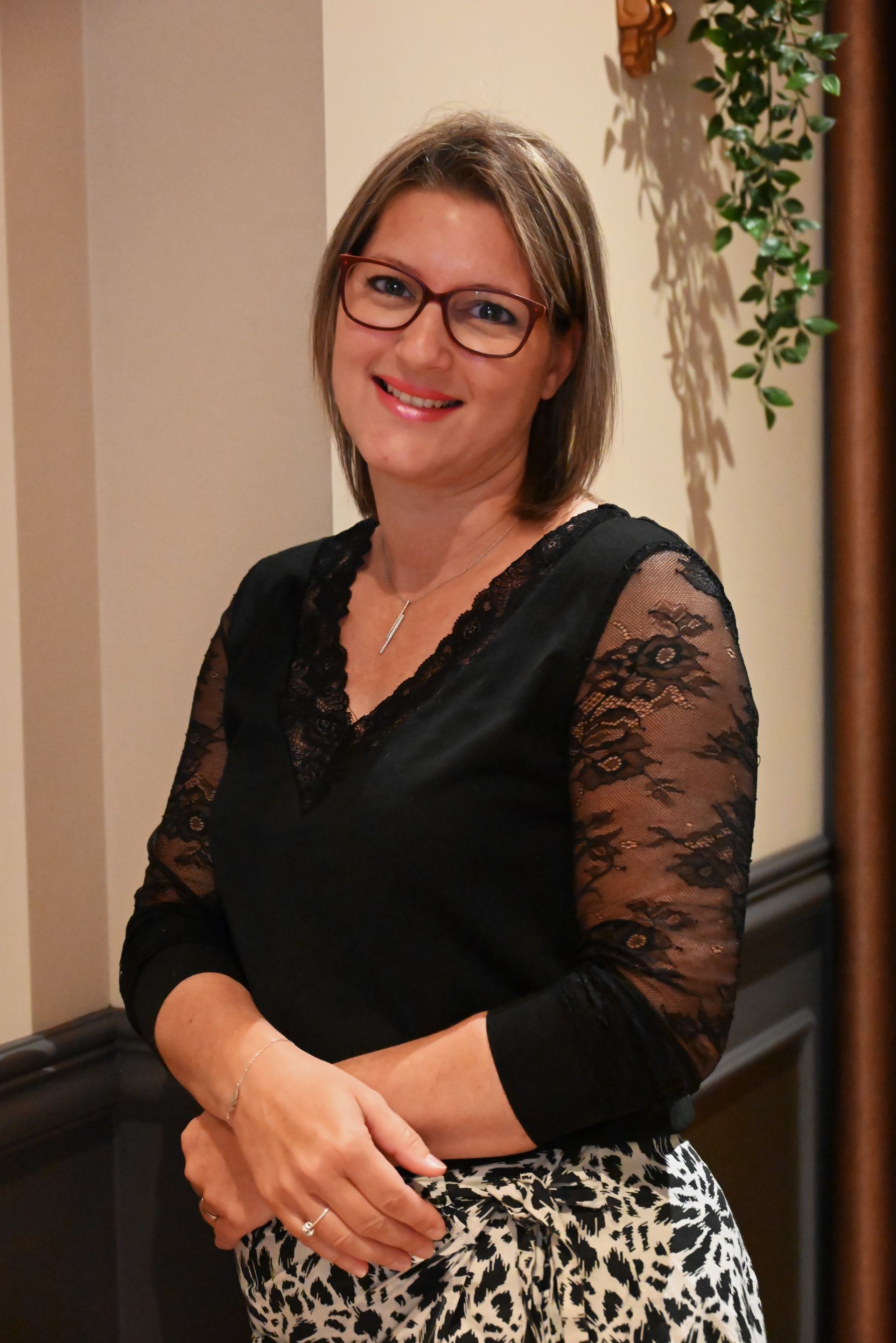 Une femme portant des lunettes et un haut en dentelle noire sourit à la caméra
