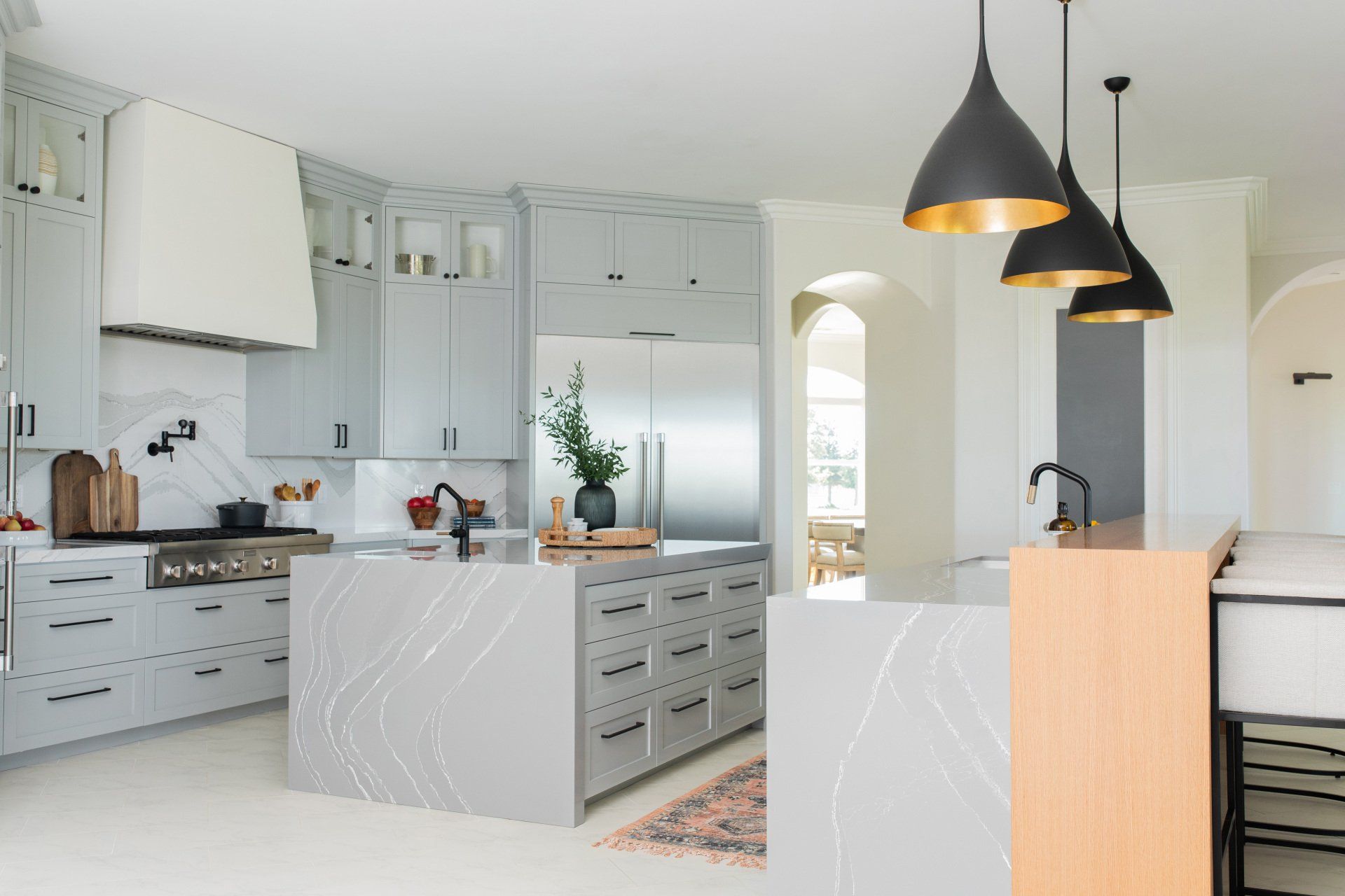 A kitchen with gray cabinets , white counter tops , stainless steel appliances , and a large island.