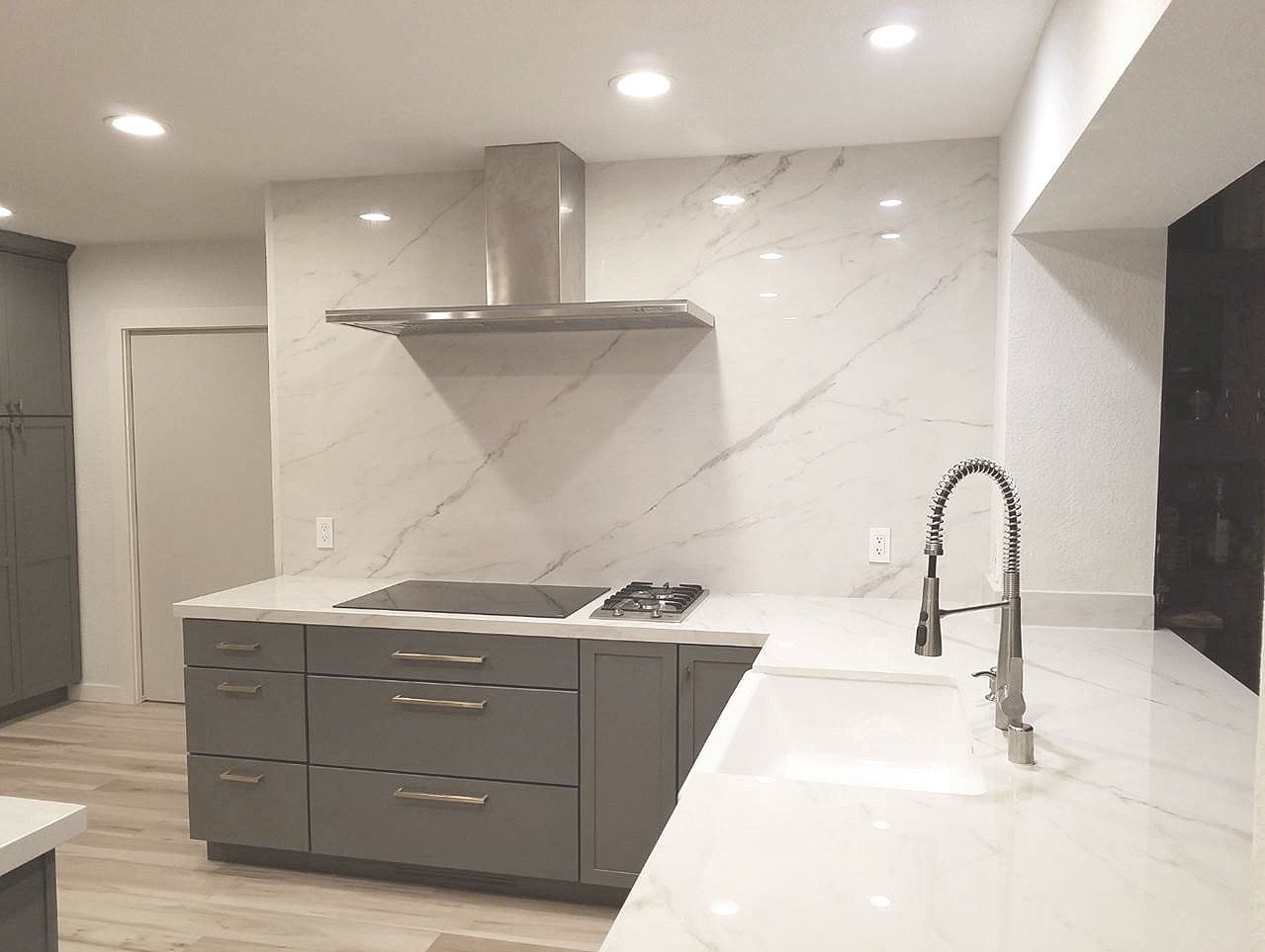 A kitchen with gray cabinets , white counter tops , a sink and a stove.