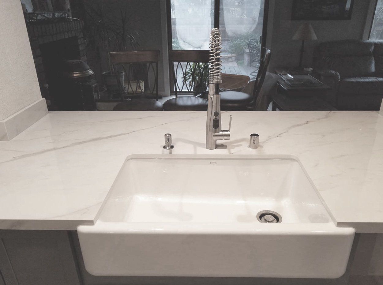 A kitchen sink with a faucet and a marble counter top.