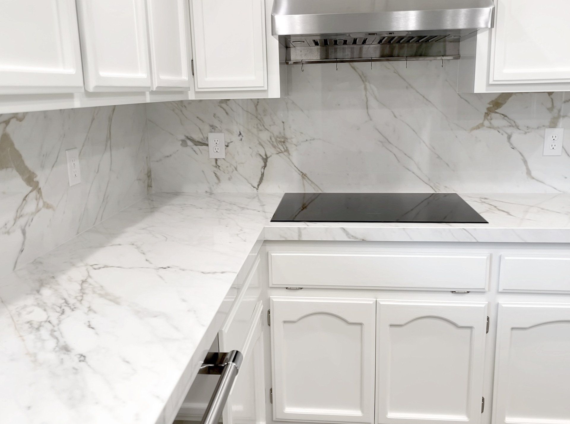 A kitchen with white cabinets , marble counter tops , and a stove top oven.