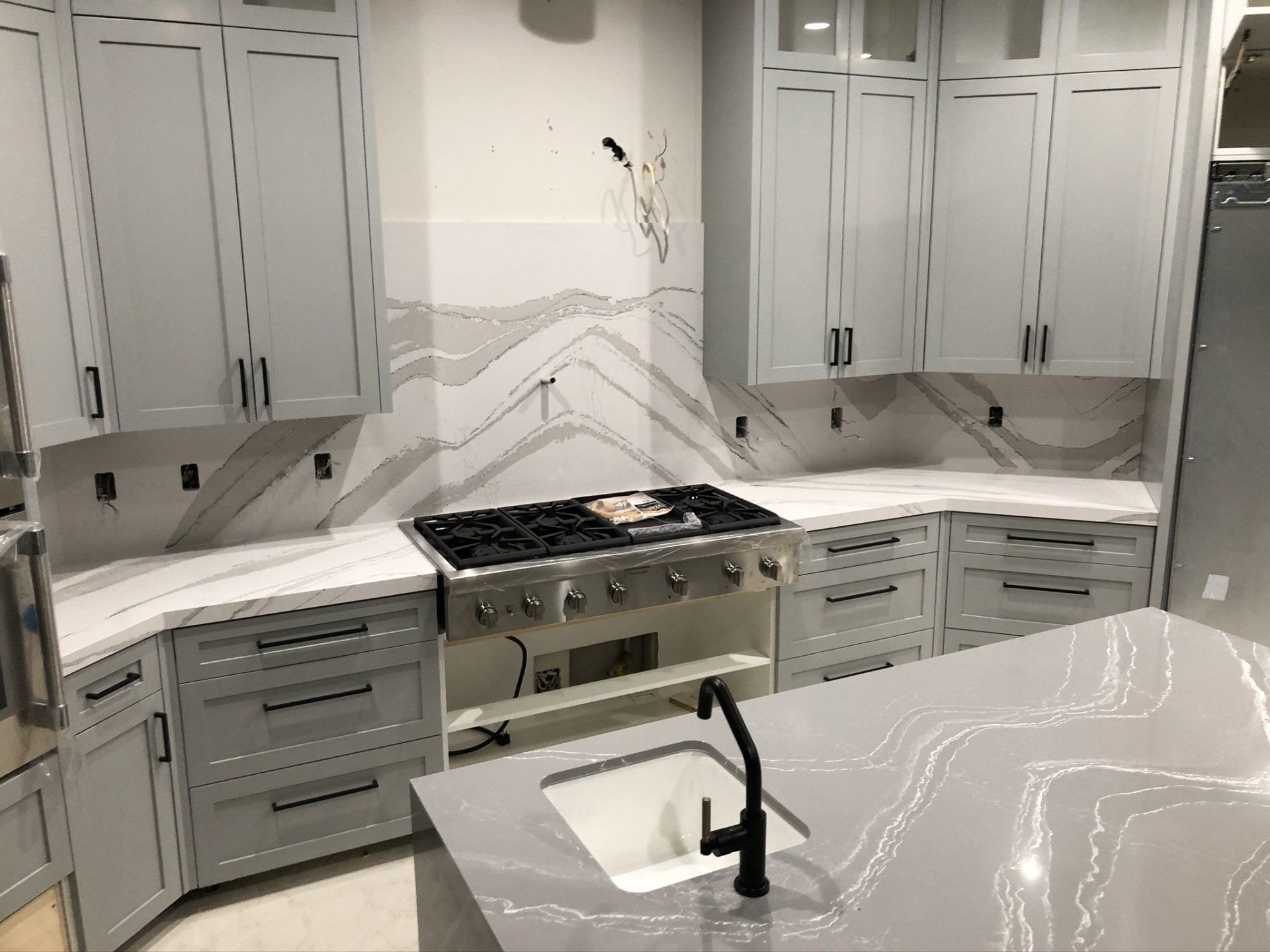 A kitchen with white cabinets , a stove , a sink , and a large island.